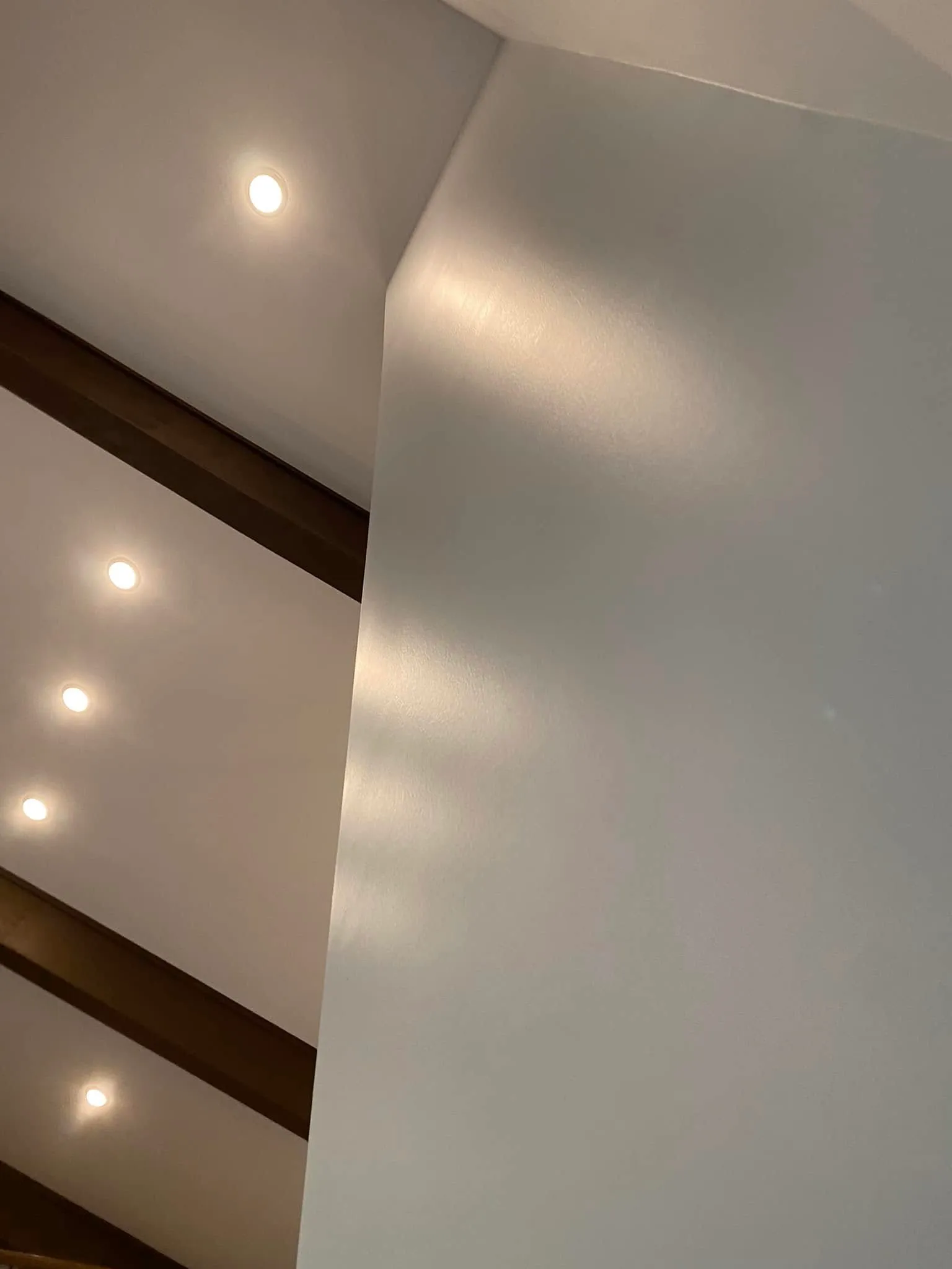Close view of a freshly painted white ceiling with recessed lights between stained wood beams.